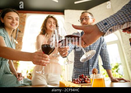 Bonnes vibrations. Les gens clinking verres avec du vin ou du champagne. Des amis heureux et joyeux célèbrent les vacances, la réunion. Gros plan sur des amis souriants, le style de vie. Faites la fête à la maison ou au restaurant, au café. Banque D'Images
