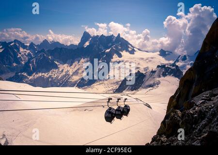 Depuis les cabines couvertes, descendre le téléphérique dans les montagnes enneigées blanches, par beau temps nuageux à Chamonix, Mont-blanc Banque D'Images