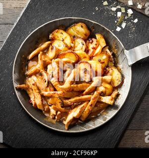 Savoureuses lanières de viande tendre servies avec de la sauce épicée dans une poêle avec des quartiers de pommes de terre dorés dans un sommet vue sur une vieille planche à découper avec assaisonnement Banque D'Images