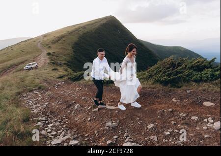 mariée et marié dans les robes de mariage marchent le long de la route avec la toile de fond des montagnes. Banque D'Images