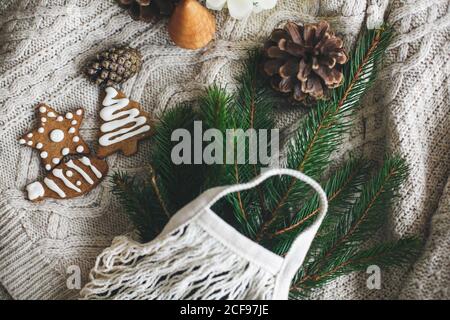 Vacances de noël sans gaspillage. Sac à provisions réutilisable avec branches d'épinette verte, biscuits de noël en pain d'épice et cônes de pin sur chandail blanc tricoté Banque D'Images