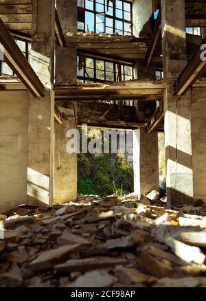 Angle bas à l'intérieur de vieux abandonné perturbé bâtiment de la ville avec les déchets sur le sol sont éclaircis par les rayons du soleil Banque D'Images