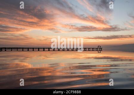 Silhouettes de personnes lointaines et méconnaissables se tenant sur la jetée près de la tranquillité lac contre ciel de coucher de soleil Banque D'Images