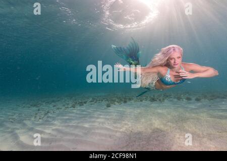 Belle petite sirène insouciante avec queue de poisson bleue nager sous l'eau mer profonde et lumineuse Banque D'Images