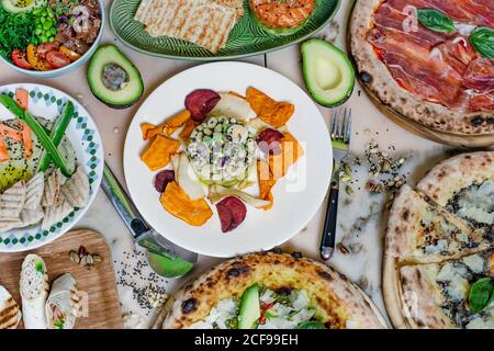 Du dessus du plat de haricots avec pétales sur l'assiette près de la fourchette avec couteau et pizza sur la table Banque D'Images