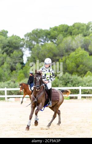 Ado garçon jockey dans casque cheval brun sur dressage arena pendant l'entraînement à l'école équestre Banque D'Images