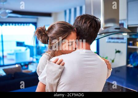 Vue latérale d'une jeune femme heureuse assise sur le comptoir de la cuisine et embrassant un mari aimant tout en passant la journée ensemble dans un appartement moderne Banque D'Images