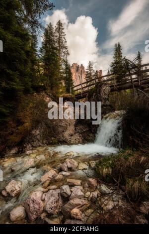 Fond rocheux avec jet d'eau mousseux coulant sous le bois pont à travers la forêt sombre dans les montagnes dans le ciel nuageux jour dedans Dolomites Italie Banque D'Images