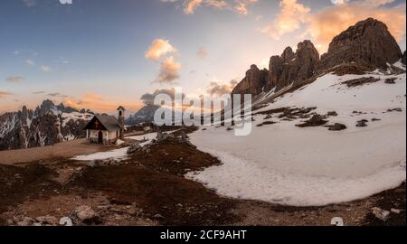 Paysage de montagne avec maison rurale située dans la vallée enneigée entourée Par danger rochers sous ciel ouvert nuageux dans les Dolomites Italie Banque D'Images