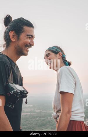 Vue latérale à angle bas de deux voyageurs en train de rire tenue décontractée debout sur fond de vert vallée paysage et se regardant l'un l'autre Banque D'Images