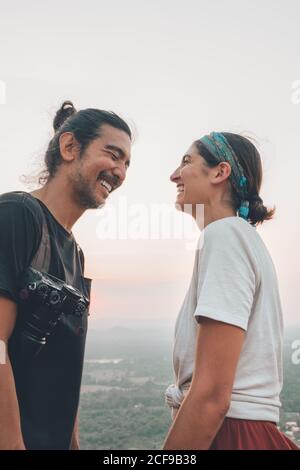 Vue latérale à angle bas de deux voyageurs en train de rire tenue décontractée debout sur fond de vert vallée paysage et se regardant l'un l'autre Banque D'Images