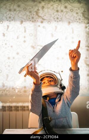 Un garçon fantastique dans un casque d'astronaute jouant avec un avion en papier à accueil Banque D'Images