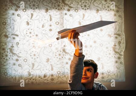 Un garçon amusé jouant avec un avion en papier avec un pétard dans la chambre Banque D'Images