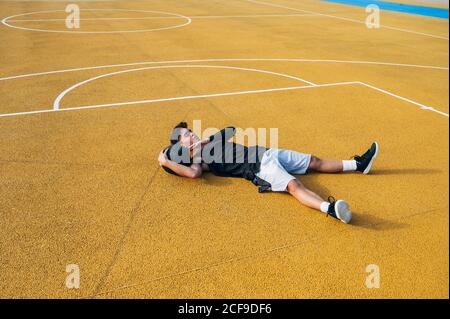 Jeune homme et ballon allongé sur un terrain de basket-ball en plein air après avoir joué au basket-ball Banque D'Images