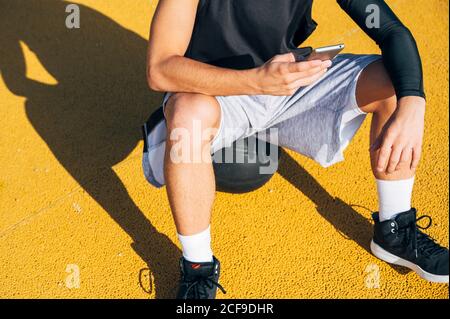 Un joueur de basket-ball masculin utilisant son smartphone se repose après une séance d'entraînement. Banque D'Images