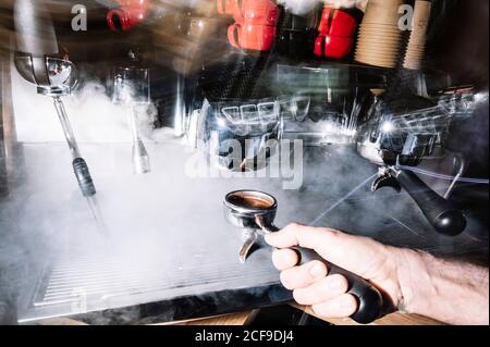 Vue latérale du barista anonyme préparant un café aromatique debout près de la cafetière professionnelle avec porte-filtre dans le café Banque D'Images