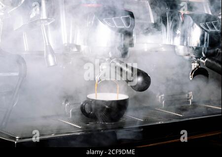 Verre avec café chaud placé sur panneau métallique de professionnel cafetière dans un café sombre Banque D'Images