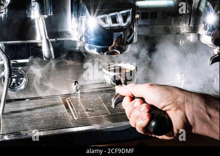 un barista anonyme prépare un café aromatique à proximité d'une cafetière professionnelle avec portafilter dans le café Banque D'Images