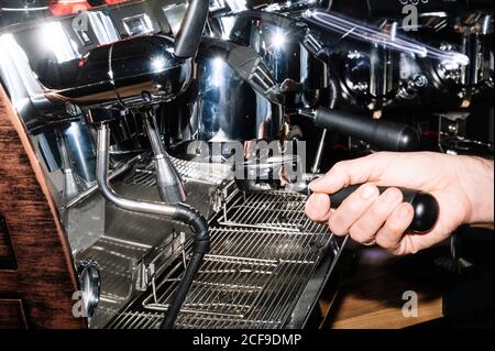 Vue latérale du barista anonyme préparant un café aromatique debout près de la cafetière professionnelle avec porte-filtre dans le café Banque D'Images