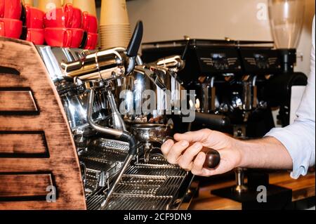 Vue latérale du barista anonyme préparant un café aromatique debout près de la cafetière professionnelle avec porte-filtre dans le café Banque D'Images