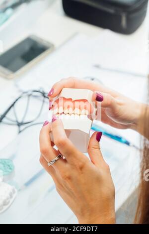 De la récolte ci-dessus, une femelle élève tenant une prothèse tout en étant assise à table pendant la classe de dentisterie Banque D'Images