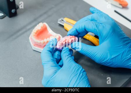 Du dessus de la récolte les mains d'étudiant mâle tenant la prothèse et la pâte assis à la table pendant le cours de dentisterie Banque D'Images