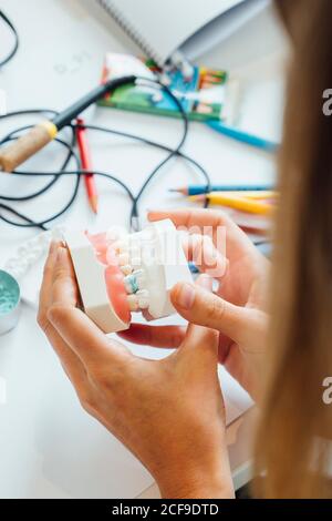 De la récolte ci-dessus, une femelle élève tenant une prothèse tout en étant assise à table pendant la classe de dentisterie Banque D'Images