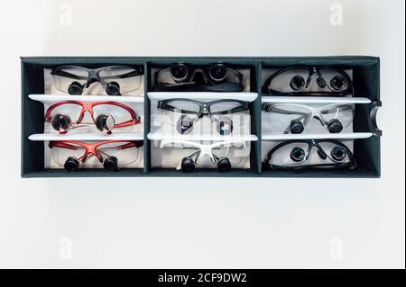 Vue de dessus des lunettes médicales pour dentiste multicolores avec lentilles binoculaires disposés dans une boîte noire placée sur une table blanche en laboratoire Banque D'Images