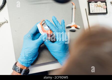 Du dessus de la récolte les mains d'étudiant mâle tenant la prothèse et la pâte assis à la table pendant le cours de dentisterie Banque D'Images