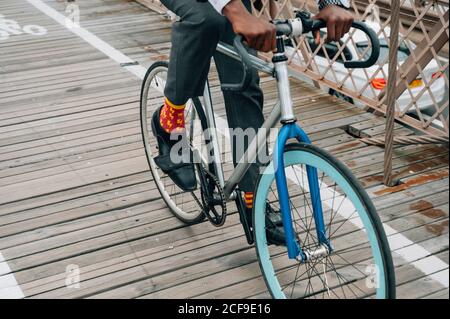 Court anonyme bien habillé homme d'affaires cycliste dans l'équitation sur le vélo Route en bois parmi la structure en métal rouge avec à New York ville Banque D'Images