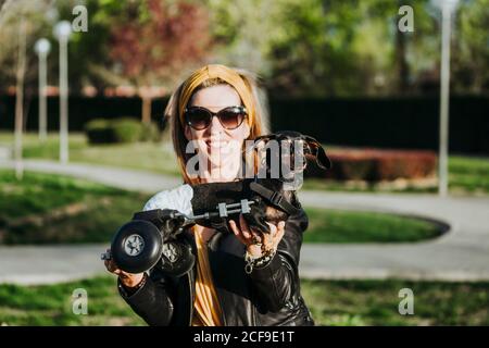 Femme souriante dans des lunettes de soleil montrant un chien handicapé paralysé de Dachshund avec fauteuil roulant dans la rue Banque D'Images