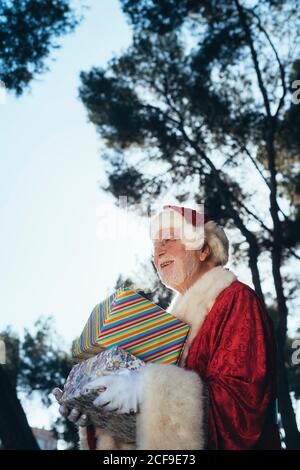 D'en haut homme joyeux en costume du Père Noël debout avec des cadeaux en minibus turquoise sur fond de nature en été vue sur l'extérieur Banque D'Images