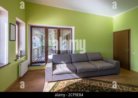 Intérieur de la maison de bureau avec des murs verts dans le cottage. Canapé gris clair. Fenêtres panoramiques. Porte en bois. Banque D'Images