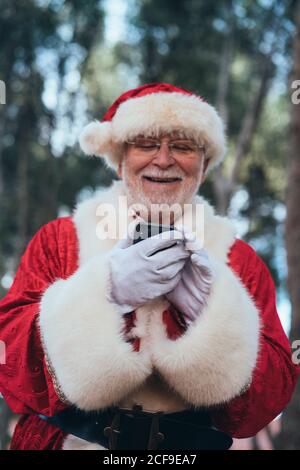 D'en-dessous, homme joyeux en costume de Père Noël en utilisant téléphone mobile moderne sur fond de nature floue Banque D'Images