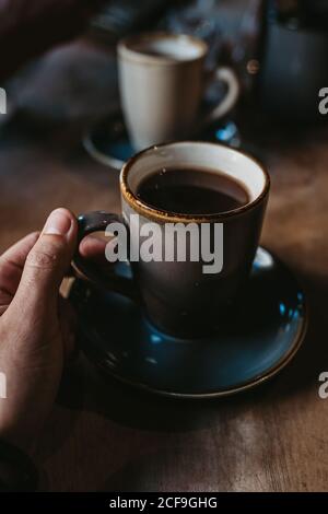 Rognez les mains d'une femme méconnue assise sur une table en bois café chaud dans une tasse rustique Banque D'Images