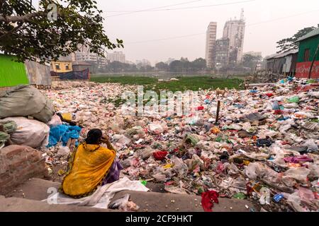 Bangladesh - janvier 19 2019 : vue arrière d'une femme ethnique non reconnaissable dans des vêtements traditionnels répondant à un appel téléphonique tout en étant assis près des ordures dans le jardin de la ville Banque D'Images
