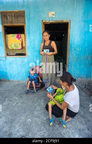 Dili, Timor oriental - 09 AOÛT 2018 : jeunes femmes asiatiques avec de petits enfants regardant des photos professionnelles dans la cour de la maison pauvre Banque D'Images