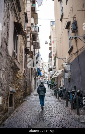 Vue arrière de la femme touristique aux cheveux noirs sans visage dans le chaud vêtements explorant la rue étroite en pierre de bloc entre les anciens bâtiments à Quartier espagnol de Naples Banque D'Images