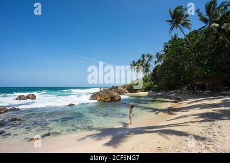 De dessus de la femme voyageur en maillot de bain appréciant la brise de mer Sur la plage de sable vide de la côte tropicale à Mirissa Banque D'Images