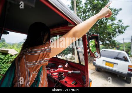 Vue arrière de la femme aux cheveux noirs sans visage dans une ambiance décontractée portez des signalisateurs à la main lorsque vous conduisez en voiture rouge traditionnelle Pousse-pousse au Sri Lanka Banque D'Images