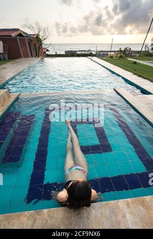De l'arrière-plan vue de la dame de repos sans visage à cheveux noirs En maillot de bain se détendre dans la piscine de Negombo Beach Hôtel à Sri Lanka Banque D'Images
