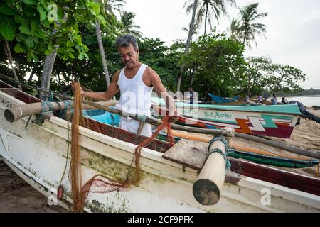 Tangalle, Sri Lanka - 28 juillet 2019 : ancien pêcheur ethnique en vêtement blanc léger préparant le filet de pêche à bord d'un bateau Banque D'Images