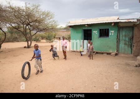 Tanzanie, Afrique de l'est - novembre, 2016: Les enfants africains en vêtements décontractés riant et jouant avec le pneu dans la cour de petite maison ancienne en Tanzanie Banque D'Images