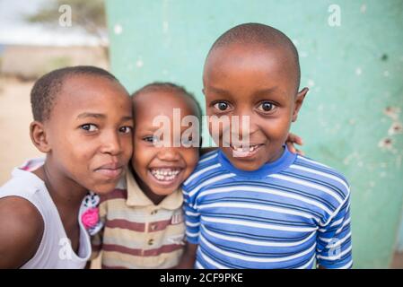 Tanzanie, Afrique de l'est - novembre, 2016: Grand angle de joyeux enfants africains dans des vêtements décontractés debout dans une étreinte et rire en Tanzanie Banque D'Images