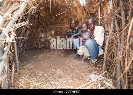 Tanzanie, Afrique de l'est - novembre, 2016: Des hommes africains en tenue décontractée avec un petit garçon assis dans une hutte faite de bâtons et regardant la caméra en Tanzanie Banque D'Images