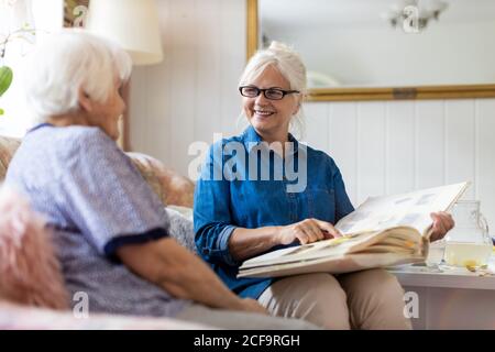 Une femme âgée et sa fille adulte regardant un album photo ensemble sur un canapé dans la salle de séjour Banque D'Images