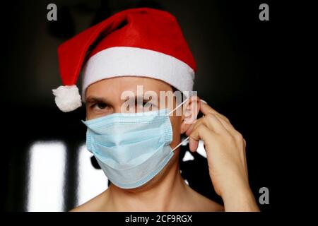 Portrait de l'homme en masque médical et chapeau du Père Noël. Célébration de Noël pendant la pandémie du coronavirus Banque D'Images