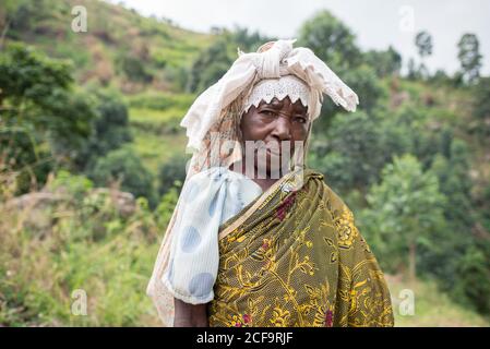 Ouganda - novembre, 26 2016: Femme africaine senior de corps entier regardant la caméra et le sac de transport sur le dos tout en marchant sur le chemin dans la forêt Banque D'Images