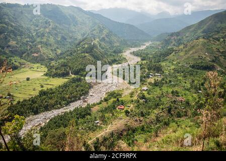 Ouganda - 26 novembre 2016: D'en haut magnifique paysage de campagne avec de petits champs cultivés et village solitaire le long de la rivière sinueuse dans la vallée de la brume parmi les collines avec l'herbe verte luxuriante et les forêts denses Banque D'Images