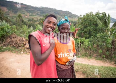 Ouganda - novembre, 26 2016: Sympathique homme noir embrassant une femme âgée regardant la caméra tout en se tenant sur l'herbe à l'extérieur du village Banque D'Images
